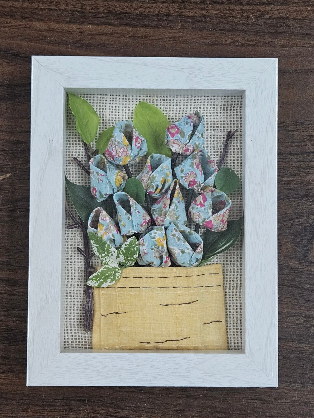 Handmade flowers with sky blue flower pots and green leaves, put them in a picture frame, flowers are made of fabric.